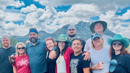 A diverse group of people in hats gathers in front of the towering Davis Mountains, enjoying West Texas